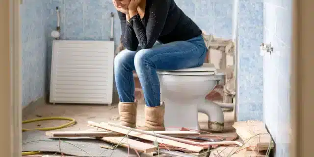 upset woman sits on toilet in demolished | Pacific Bay Construction